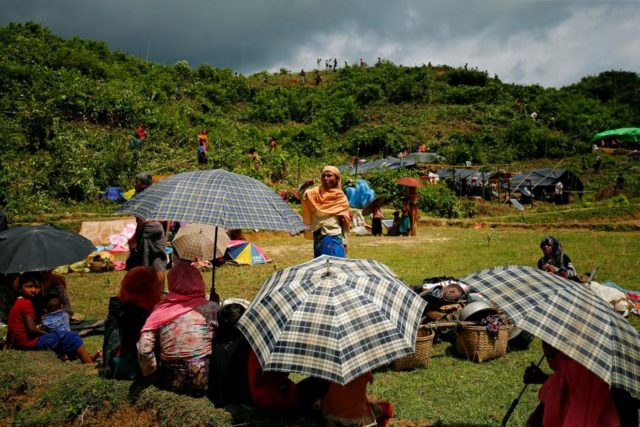 New Rohingya refugees sit on the ground as others clean bushes off of a hill to build makeshift shelters in Balukhali near Cox’s Bazar