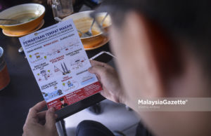 Seorang pelanggan membaca risalah pewartaan tempat larangan merokok semasa tinjauan lensa MalaysiaGazette. foto SYAFIQ AMBAK, 01 JANUARI 2019