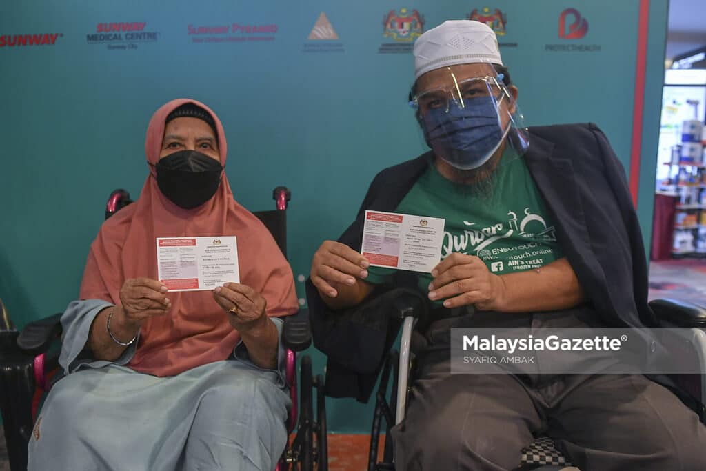 Warga emas, Siti Amun Md Amin, 85 (kiri) bersama anaknya, Abdul Razak Abdul Hamid, 60 (kanan) menunjukkan kad vaksinasi Covid-19 selepas hadir secara “walk in” untuk menerima suntikan vaksin di Pusat Pemberian Vaksin (PPV) Sunway Pyramid, Selangor. Foto SYAFIQ AMBAK, 17 JULAI 2021.