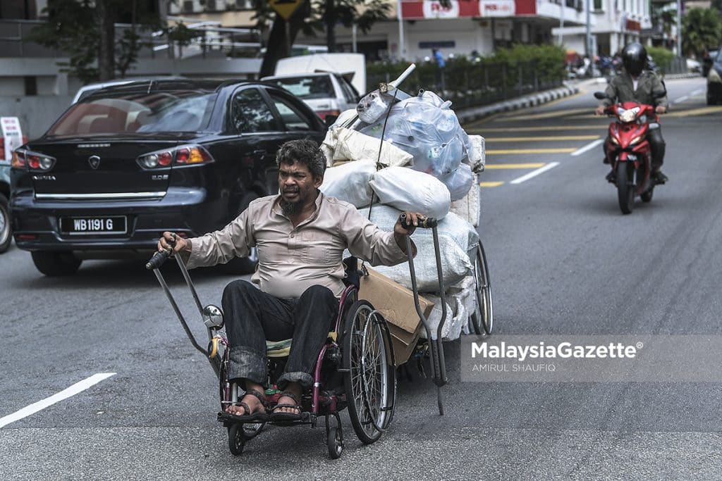    With all his strength, Affendi Muda hauls the recyclable items with his wheelchair to support his living.  PIX: AMIRUL SHAUFIQ / MalaysiaGazette / 12 APRIL 2022.